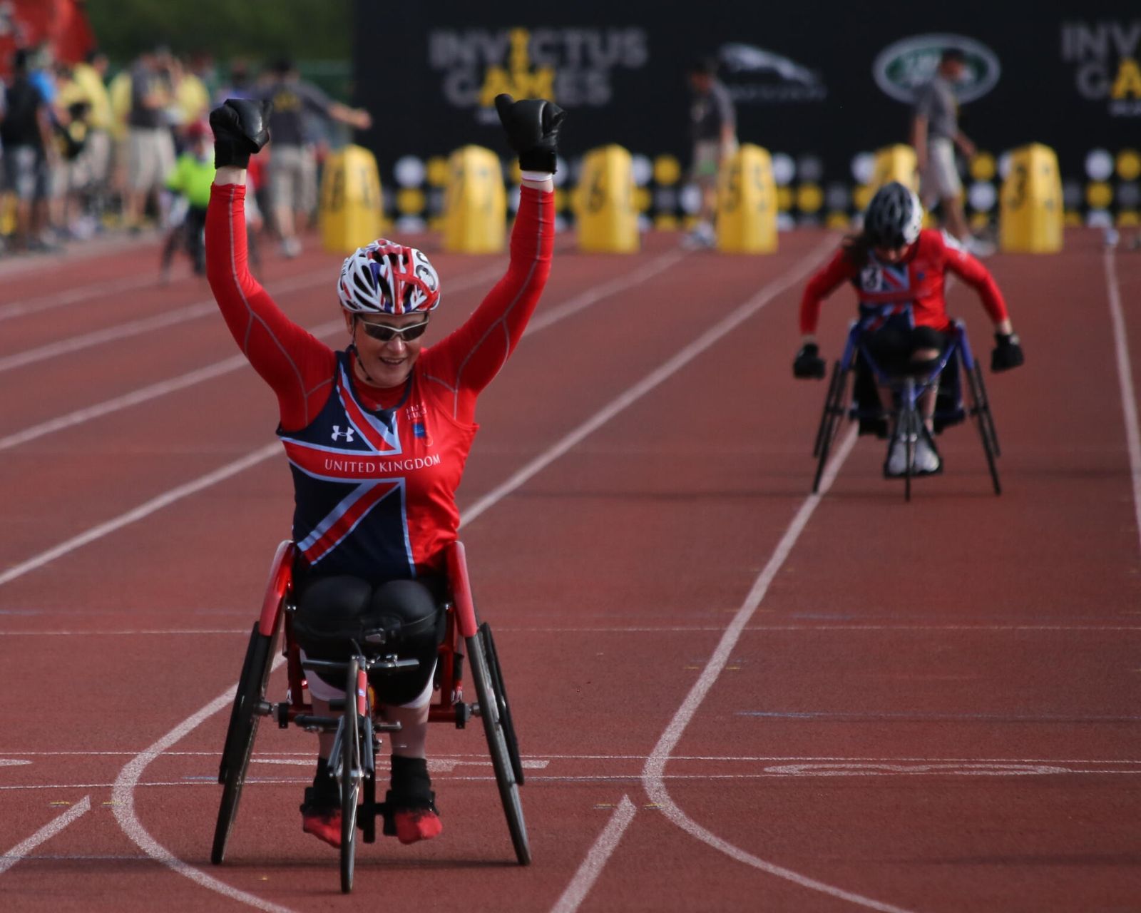A wheelchair racer crossing the finish line with both arms raised in celebration.