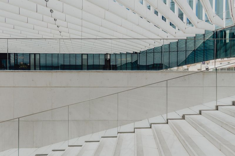 Wide concrete steps beside a long, gently sloped ramp with a glass guardrail.
