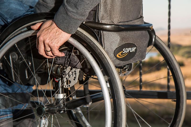 An older man's hand, wearing a wedding ring, gripping the wheel of his wheelchair.